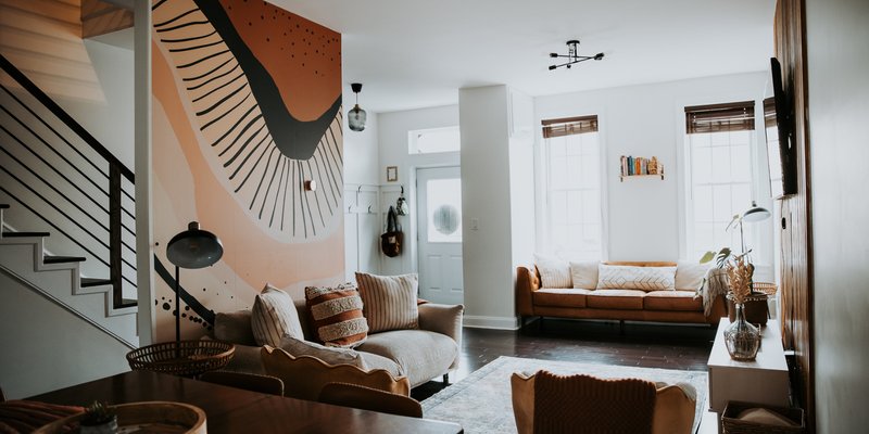 Modern, Instagram-worthy living room at Luxury on Lemon Airbnb in Lancaster, PA featuring a neutral sofa with rust accents, abstract mural wall, cozy seating area, and open layout ideal for a bachelorette weekend stay.
