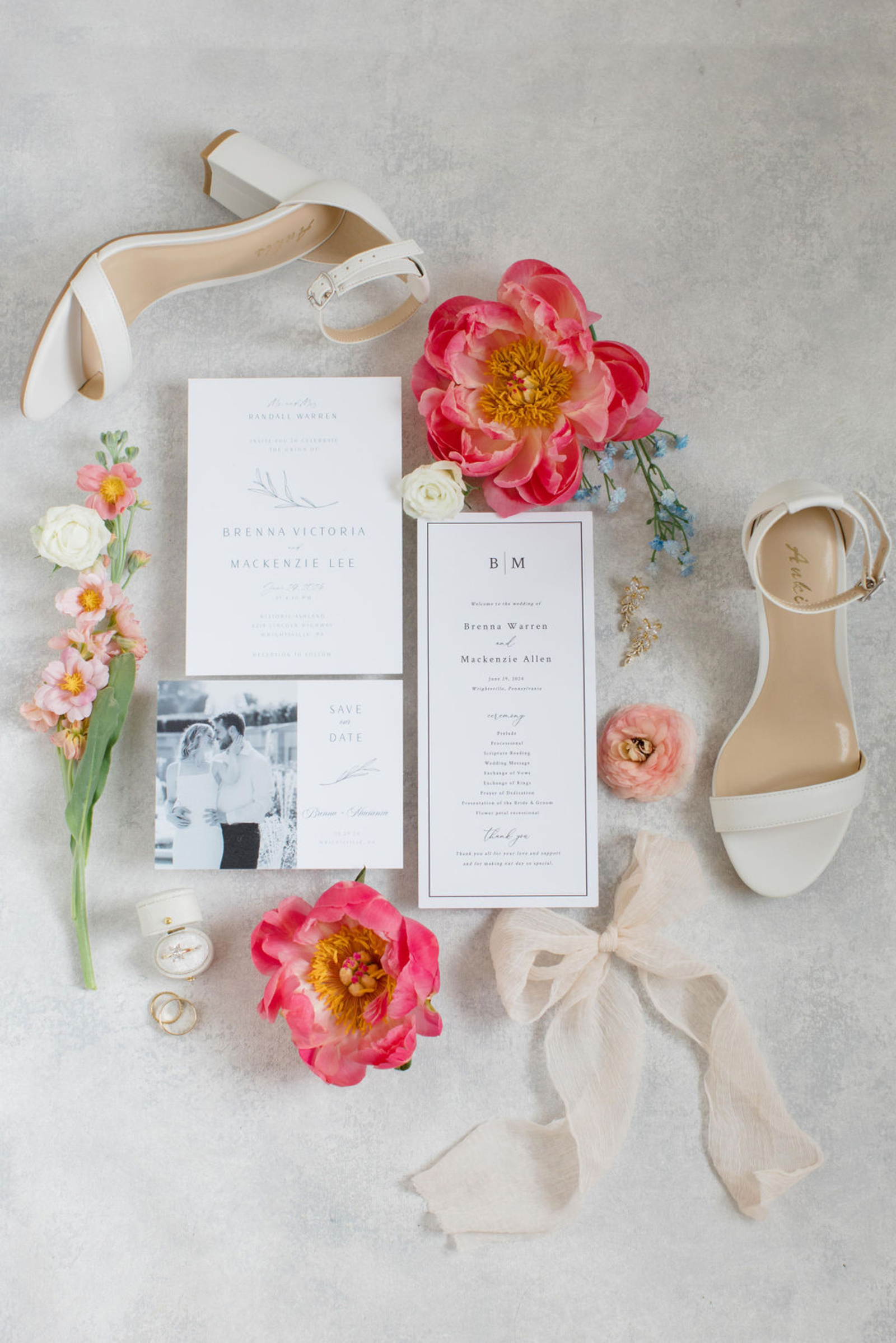 Wedding flat lay with bridal shoes, engagement ring, invitation suite, ribbon, and pink florals styled for wedding detail photos.
