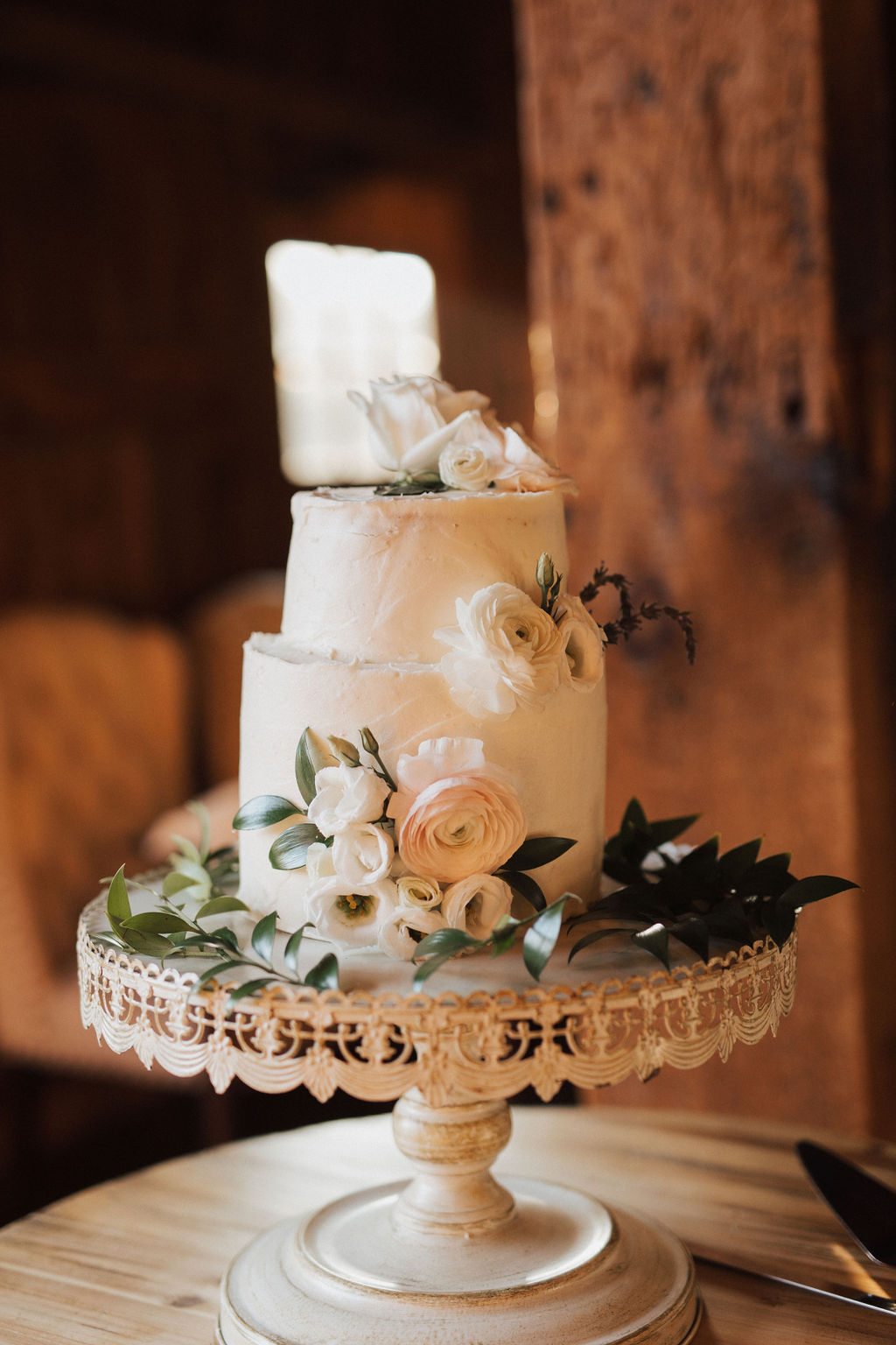 Two tiered white cake adorned with pink and white flowers on top of a white vintage cake stand