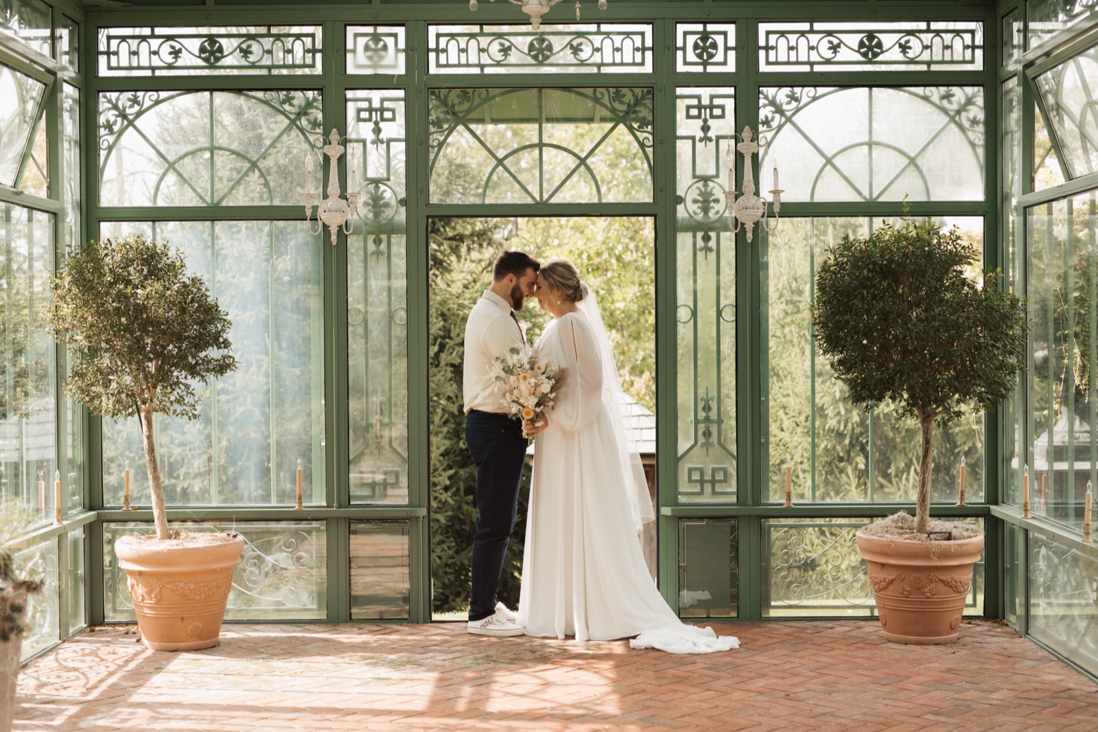 Bride and groom standing face to face in a green room full of windows