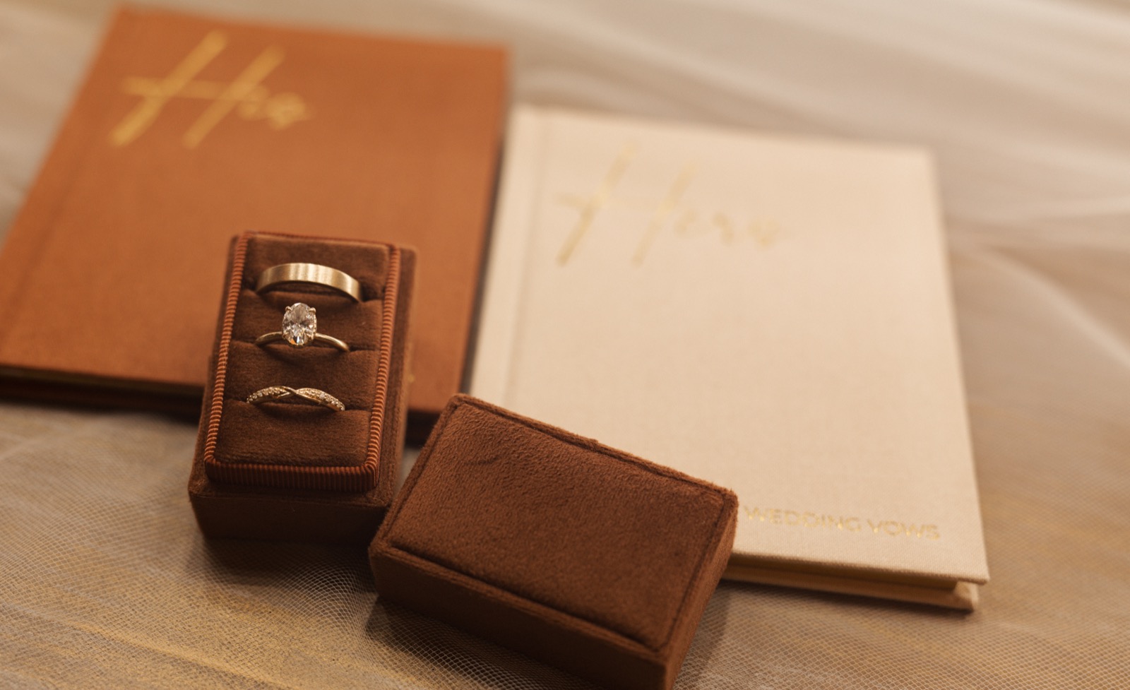 Burnt orange ring box with a oval diamond engagement ring placed between two gold bands
