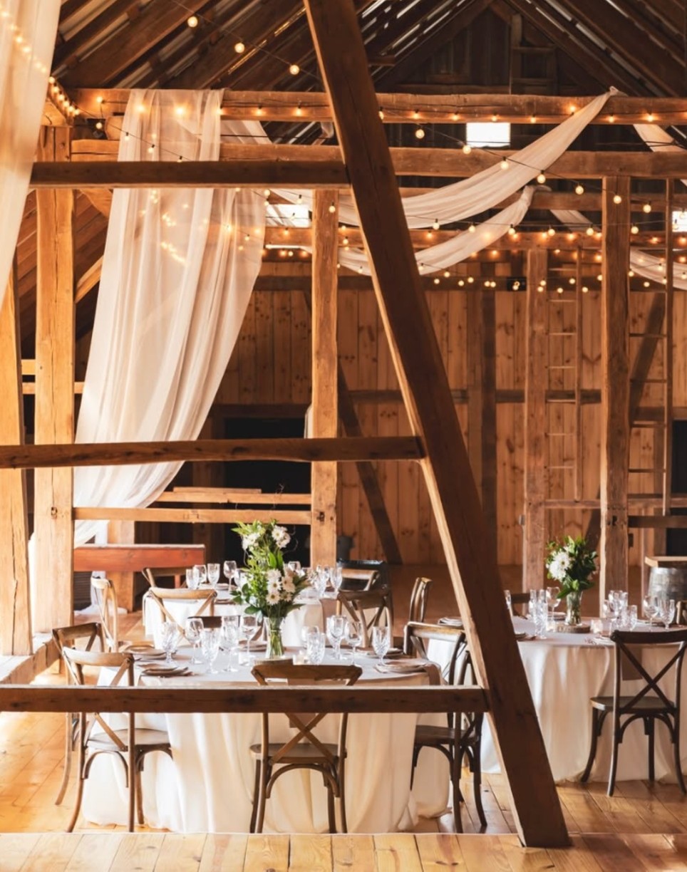 Rustic Barn Wedding Reception at the Barn at Hill Country in Gettysburg PA Rustic barn at the Barn at Hill Country wedding reception with exposed wood beams, string lights, white draping and floral centerpieces.