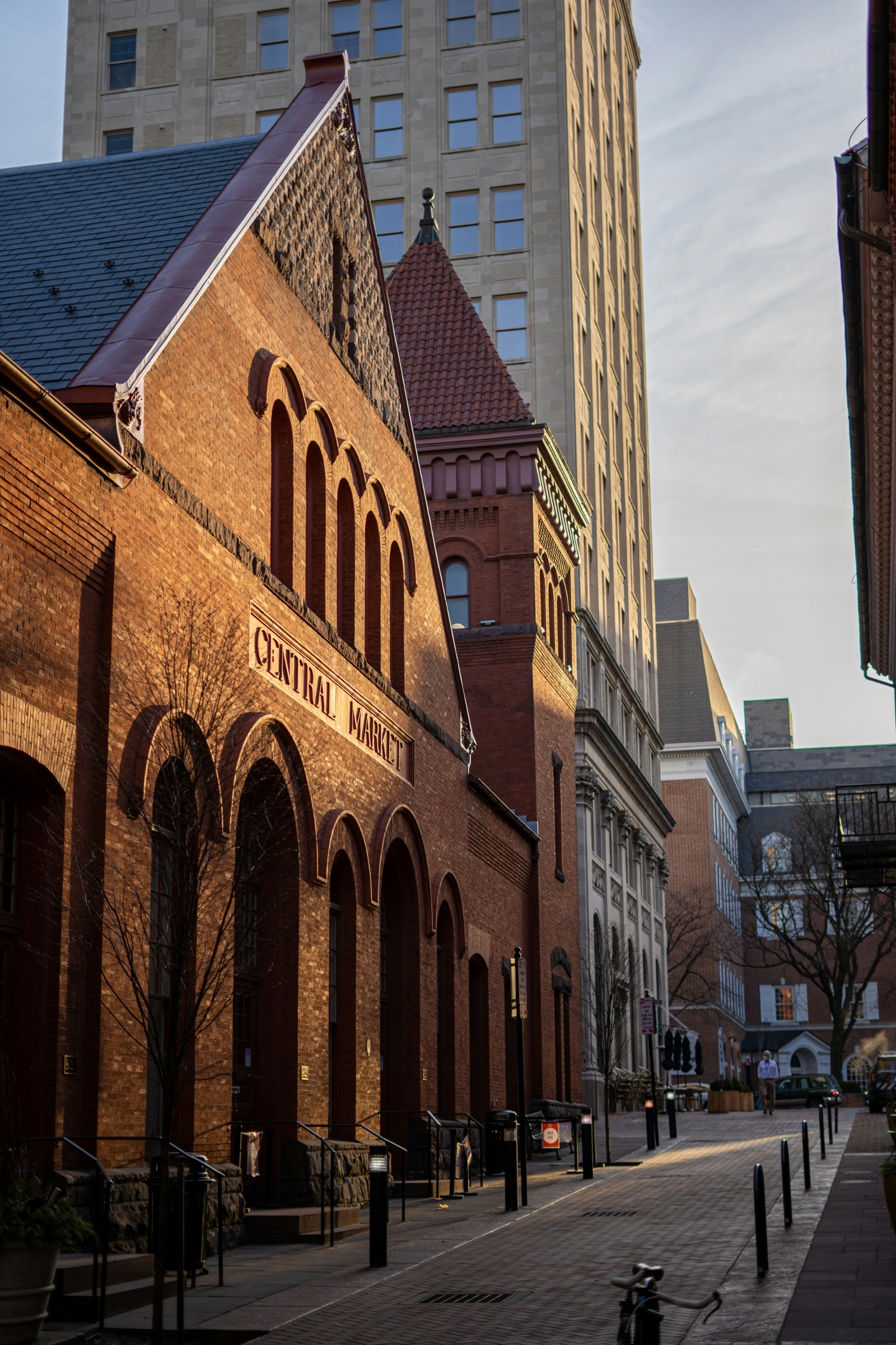 Historic Lancaster, PA brick building labeled "Central Market" with arched windows, set against a tall modern office tower in an urban street, bathed in soft morning light.