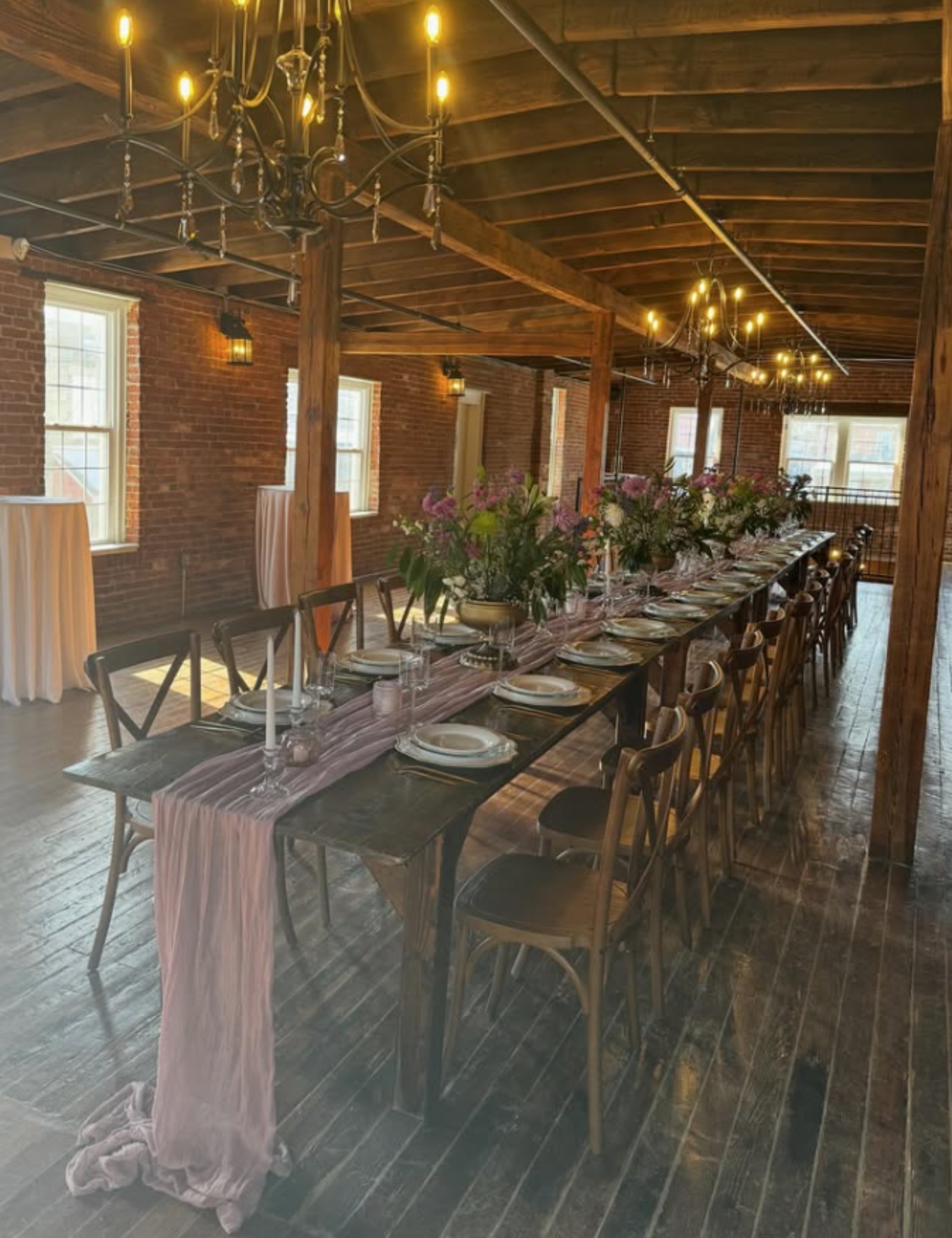 Industrial Wedding Reception at Evermore Events in Lancaster, PA Long wedding reception table decorated with pink floral arrangements, candles, and wooden chairs inside Evermore Events in Lancaster, PA.