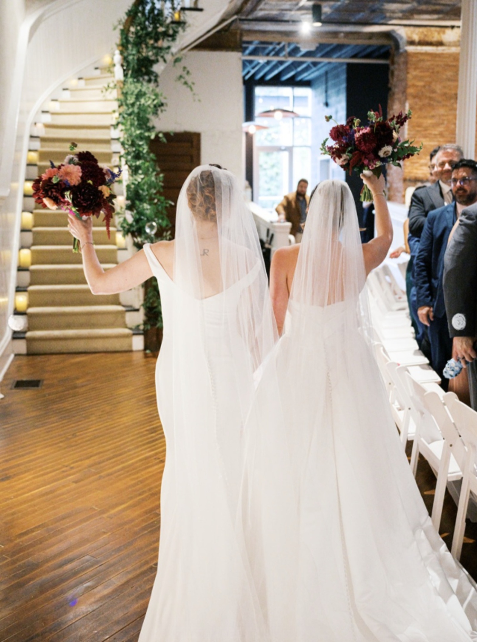 Intimate Wedding at Excelsior in Lancaster, PA Two brides celebrating inside Excelsior in Lancaster, PA, with wooden floors, a curved staircase, and exposed brick walls.