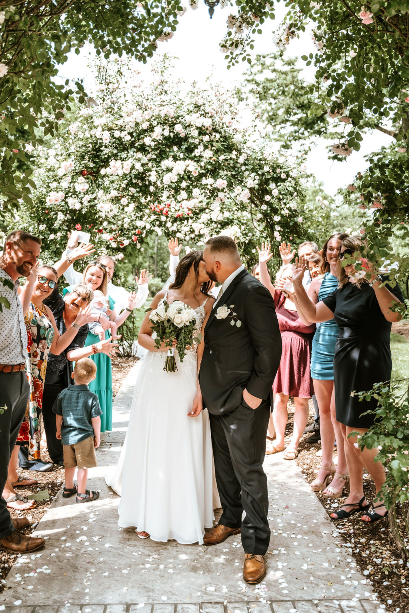 Bride and groom kissing under a blooming rose arch during an outdoor garden wedding ceremony at Moonstone Manor