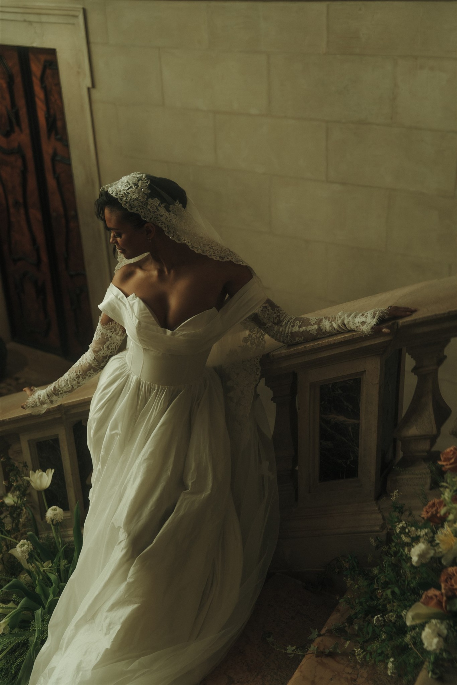 Bride in an off-the-shoulder gown with lace sleeves and a delicate lace wedding veil in a romantic indoor setting