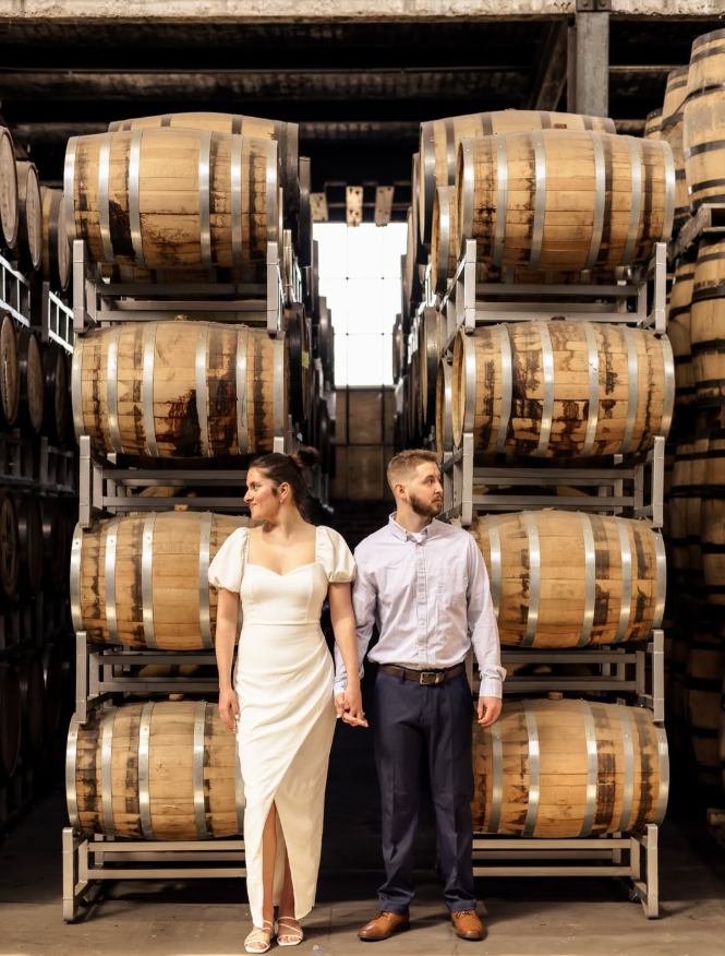 Couple walking between bourbon barrels inside The Hidden Still in Hershey, Pennsylvania, a unique rehearsal dinner restaurant and distillery.