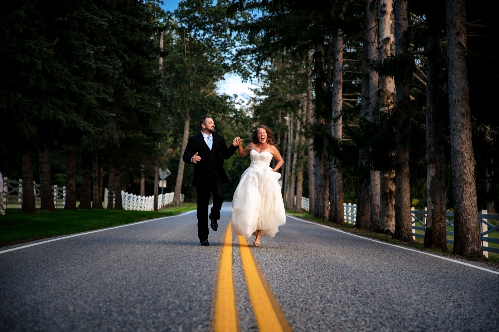 Fun Wedding Portrait on a Tree-Lined Road Bride and groom run hand in hand down a tree-lined country road during playful wedding portraits at a Pennsylvania wedding venue.