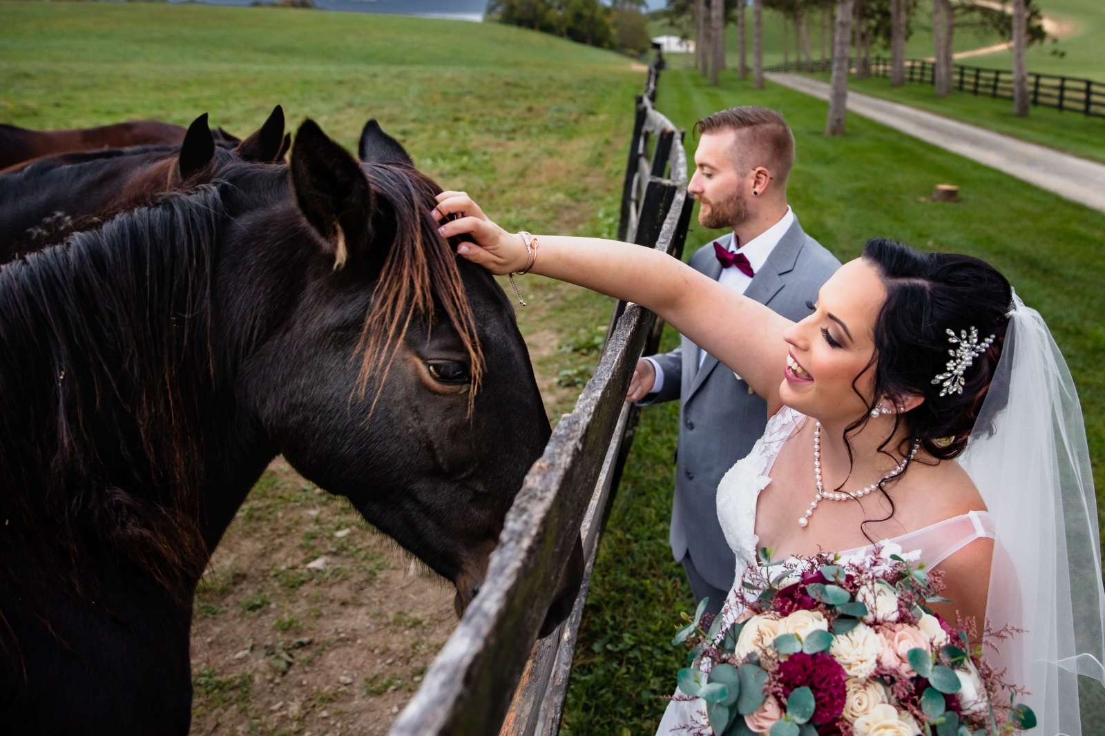 Bride and Groom with Horses Newlyweds pet horses over a fence during wedding portraits at a countryside Pennsylvania wedding venue.