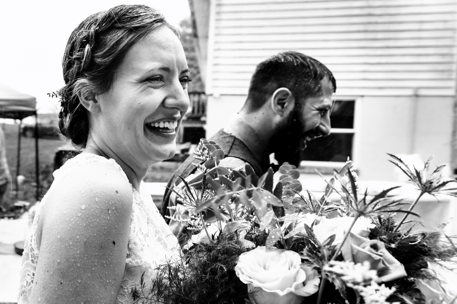 Joyful Rainy Wedding Day Portrait Bride laughs in the rain beside her groom during a backyard wedding, capturing a candid and joyful moment.