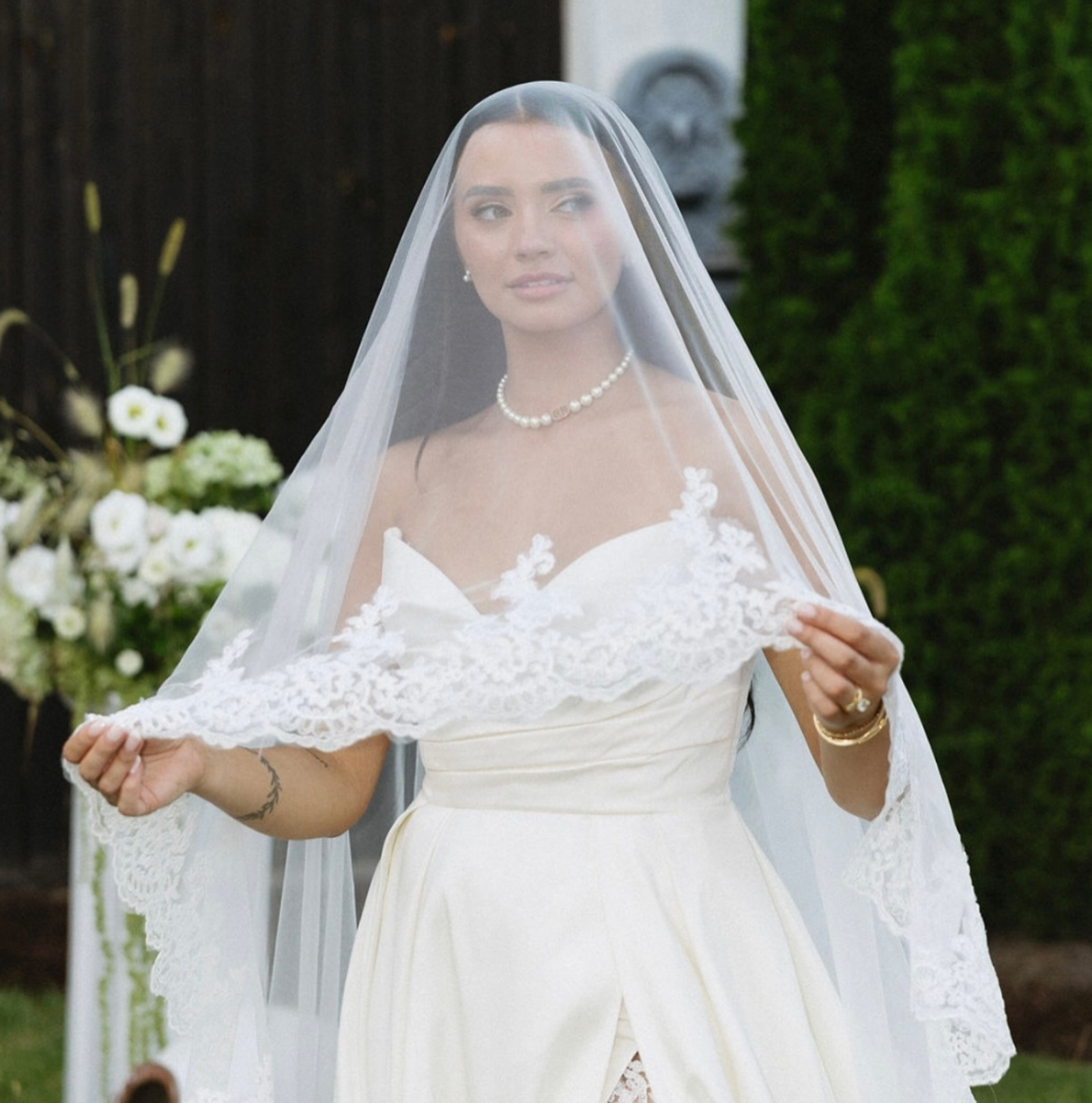 Bride wearing a lace-edged wedding veil with floral trim draped over her face for a soft romantic bridal look