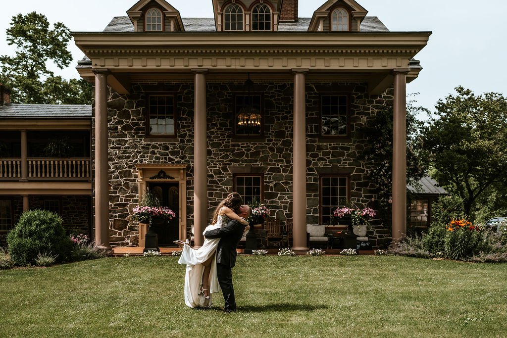Groom lifting up bride and kissing her on the lawn of grand stone building with columns