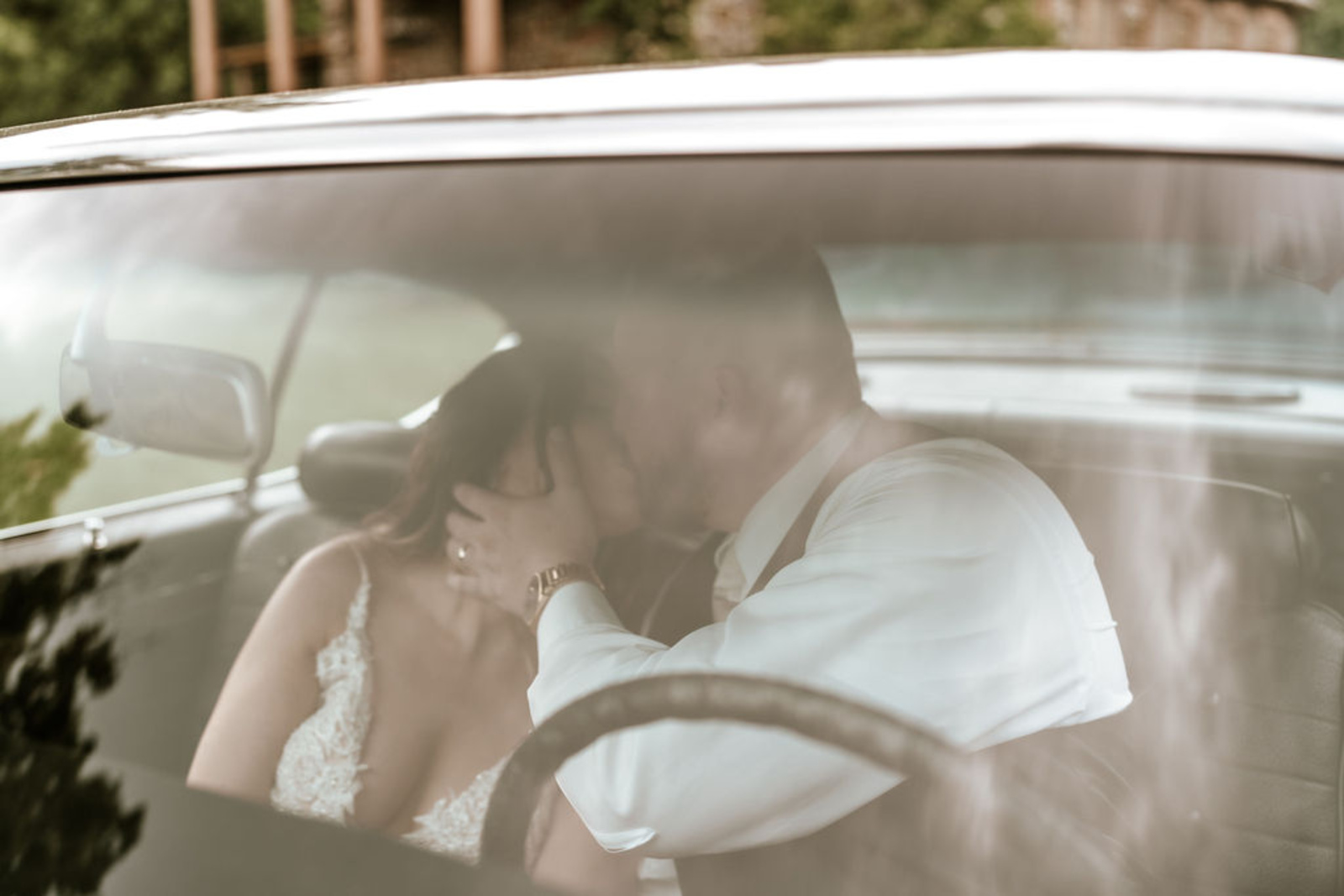 Bride and groom share a romantic kiss inside their vintage getaway car, captured through the window for a cinematic Moonstone Manor moment.