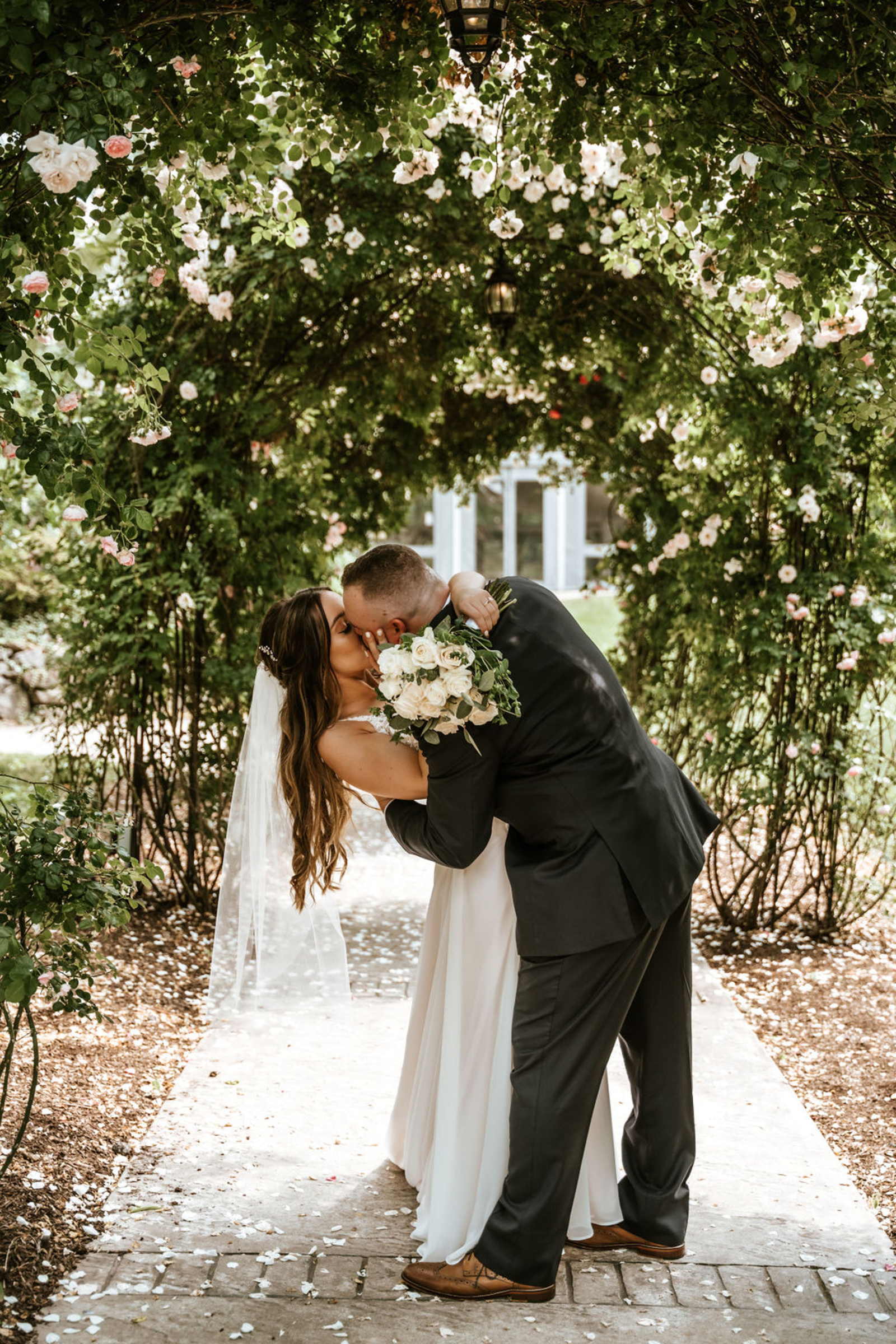 Bride and groom kissing under a rose-covered arbor at a garden wedding venue in Lancaster PA