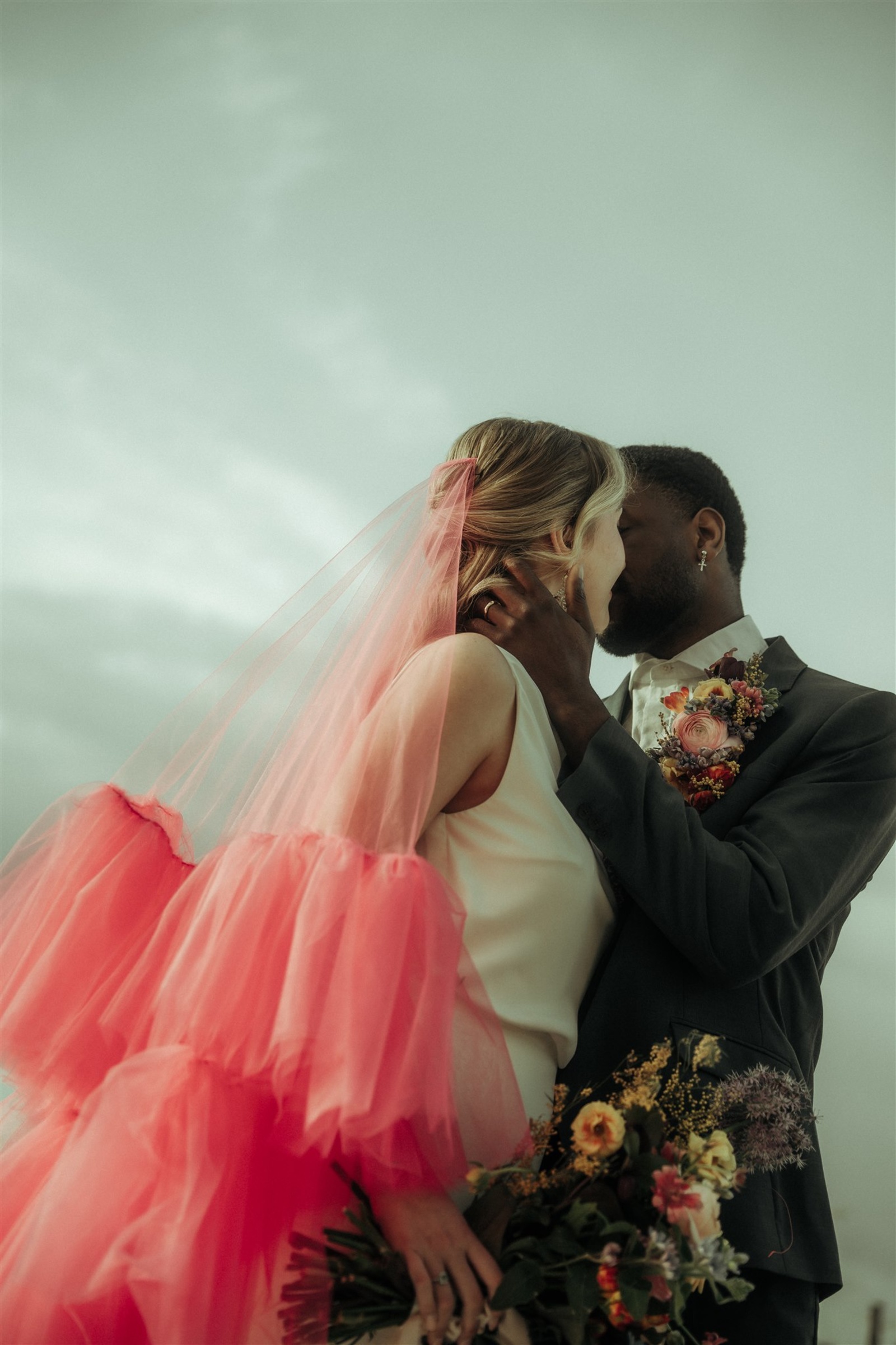 Bride and groom sharing a kiss with a soft pink tulle wedding veil creating a modern romantic bridal moment