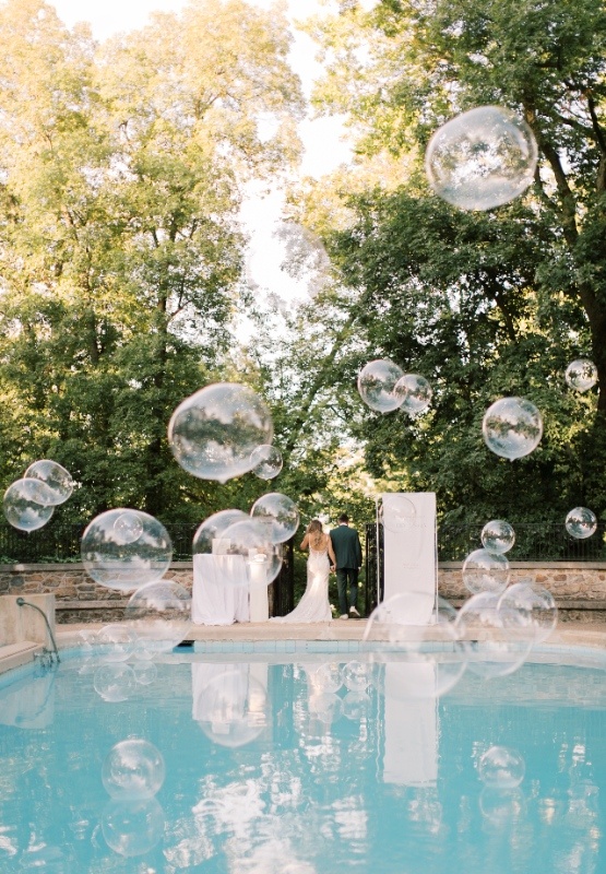 Playful Outdoor Wedding Reception with Interactive Details Outdoor wedding reception by a pool with oversized bubbles floating through the air, showcasing a fun and interactive guest experience at a Central PA wedding.
