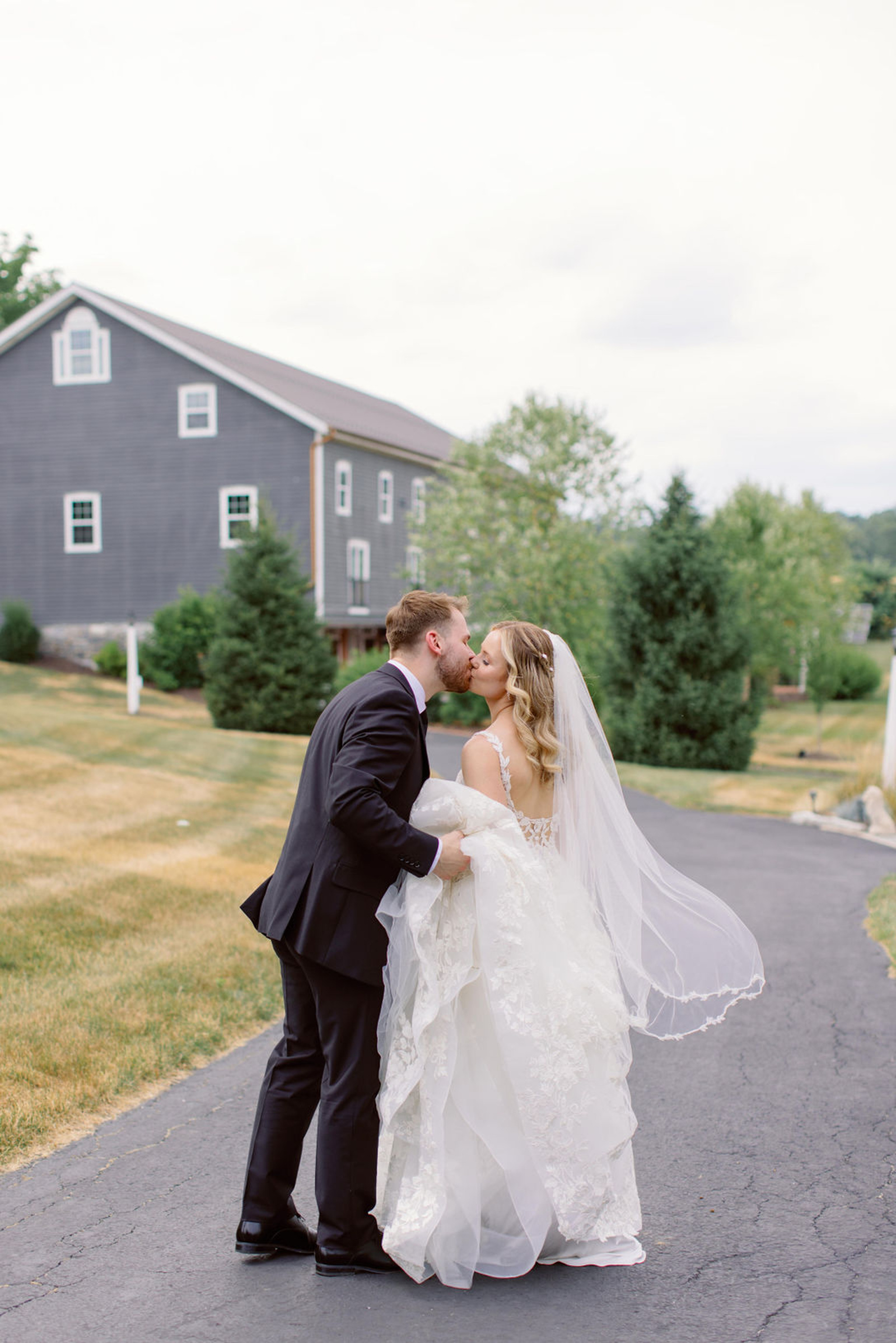 Bride and Groom Portrait Outside Historic Ashland Bride and groom kissing on the driveway outside Historic Ashland with the reception barn in the background during their summer wedding portraits.