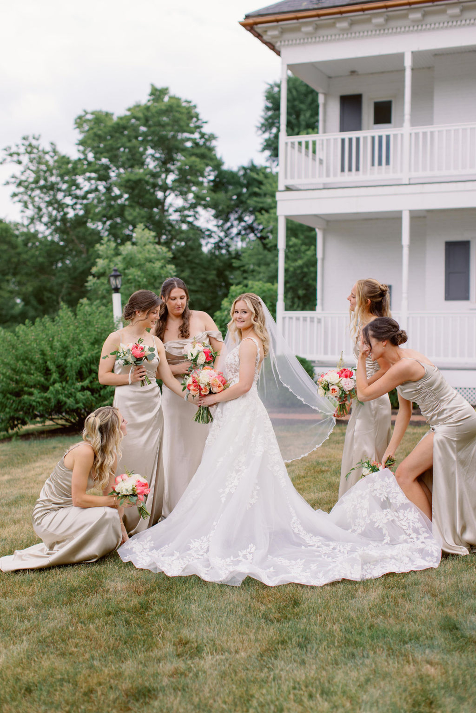 Bride with Bridesmaids at Historic Ashland Bride posing with bridesmaids in champagne satin dresses outside Historic Ashland during an early summer wedding in Pennsylvania.