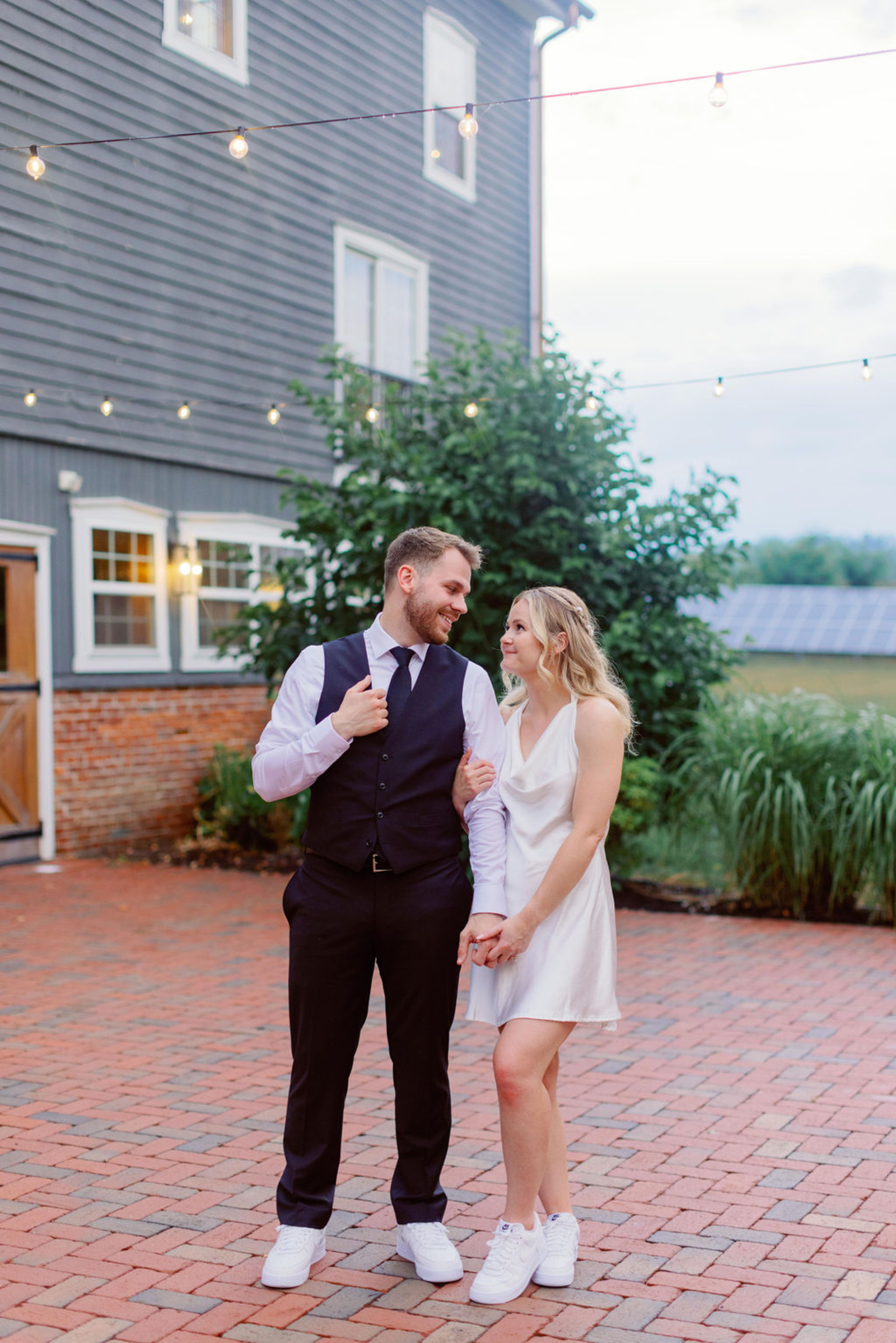 Evening Portraits at Historic Ashland Bride and groom in reception outfits walking hand-in-hand outside Historic Ashland under string lights at dusk.