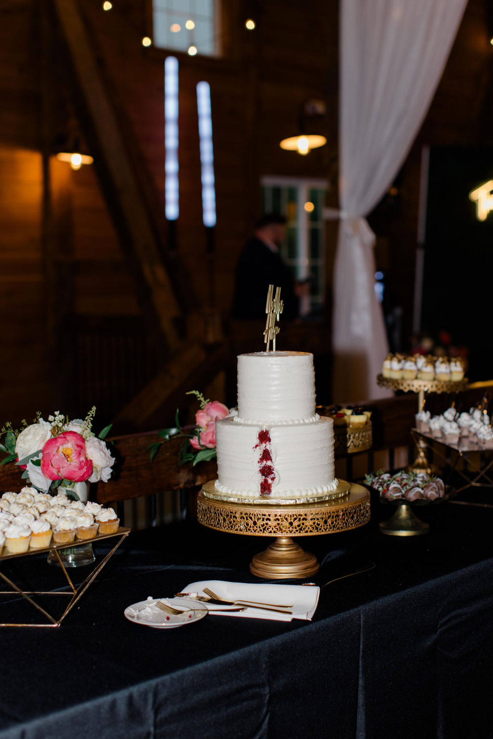 Wedding Cake and Dessert Display at Historic Ashland White wedding cake with pink florals and desserts displayed inside Historic Ashland’s candlelit barn reception space.