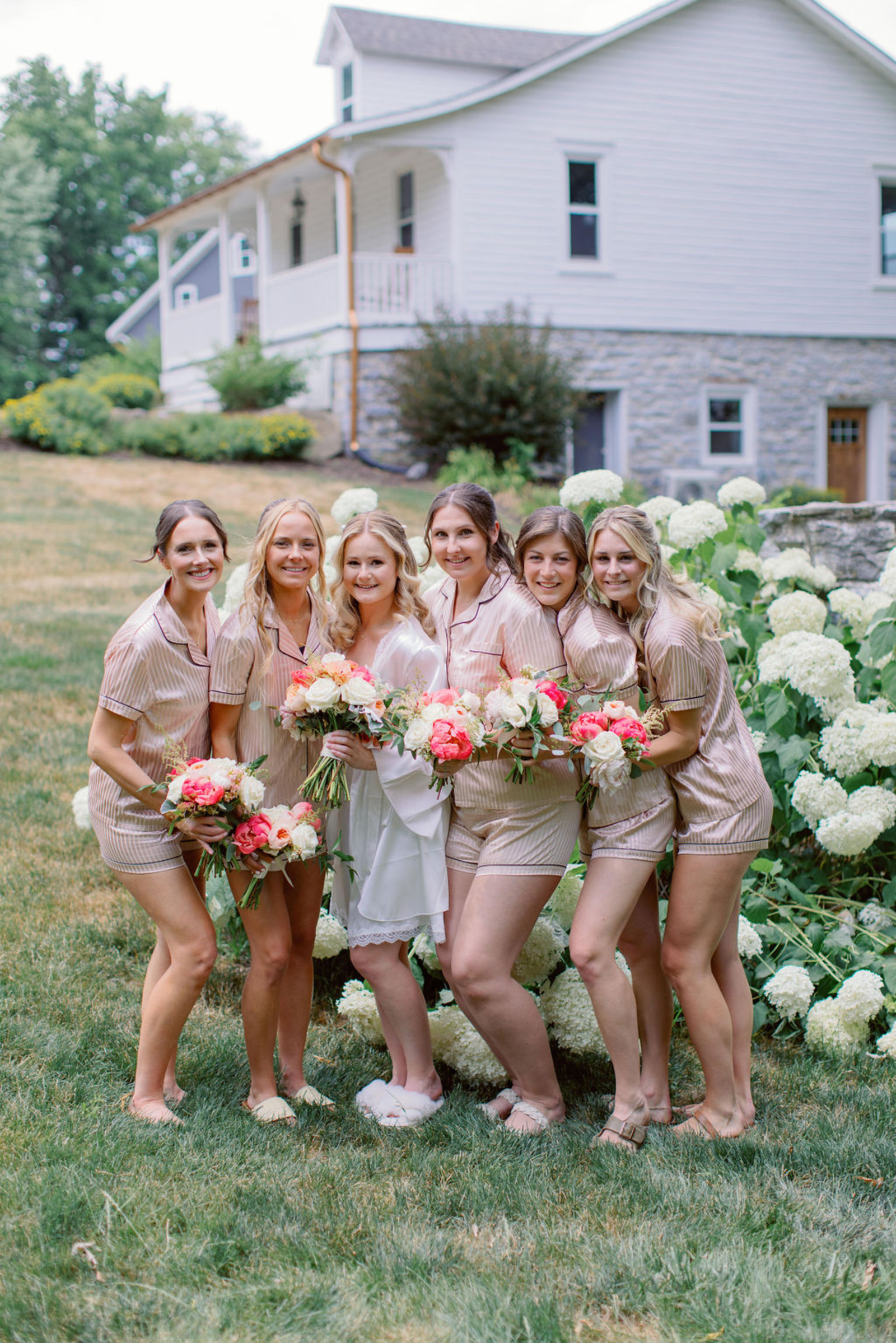 Bridesmaids Getting Ready at Historic Ashland Bride and bridesmaids in matching champagne-toned pajamas holding colorful summer bouquets outside Historic Ashland before the wedding ceremony.