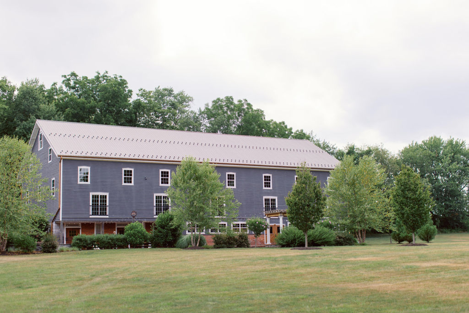 Historic Ashland Reception Barn in Pennsylvania Exterior view of Historic Ashland’s reception barn surrounded by greenery during an early summer wedding in Central Pennsylvania.