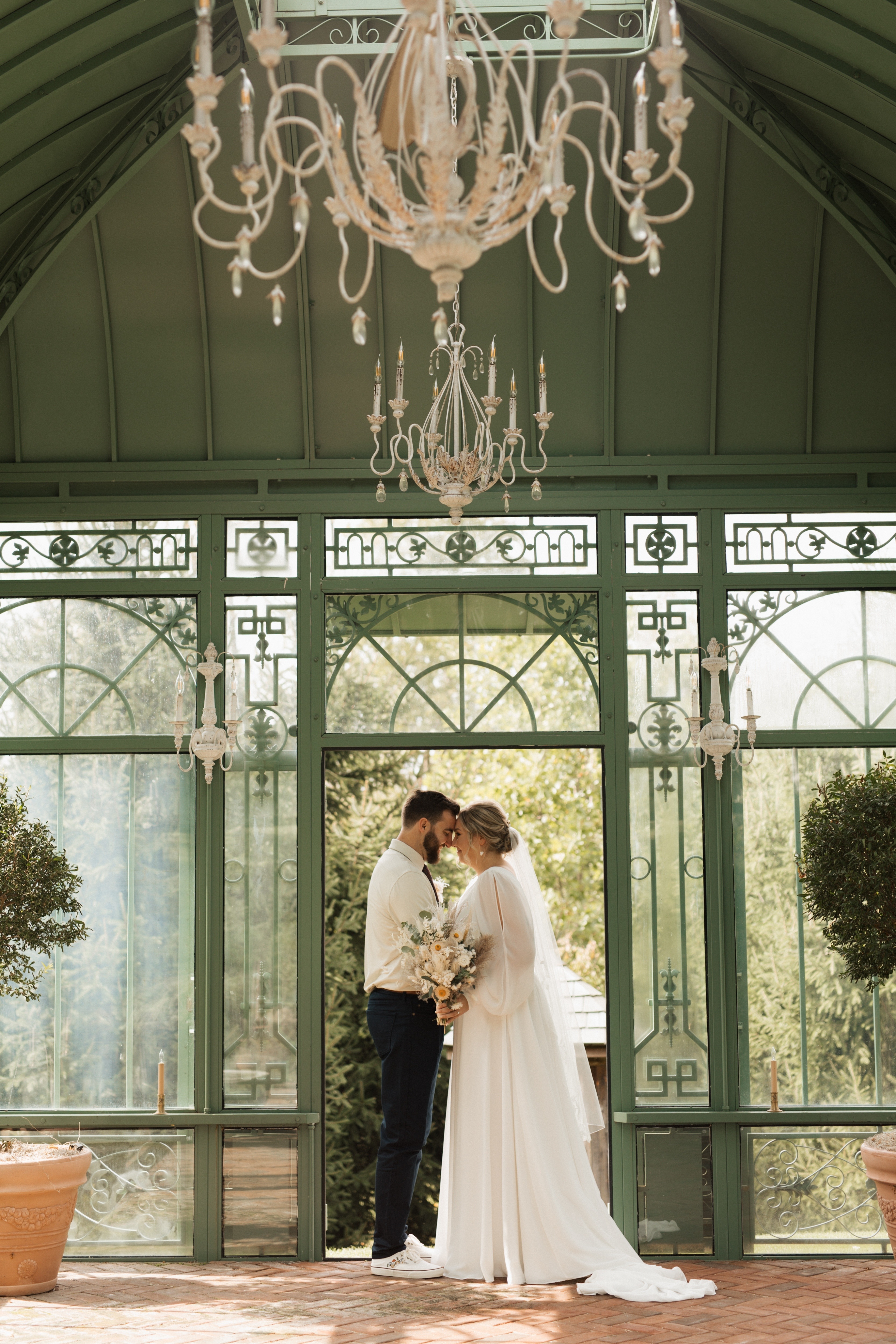 Bride and groom standing inside a greenhouse with chandeliers during a romantic garden wedding ceremony at St. Michael's Vineyard