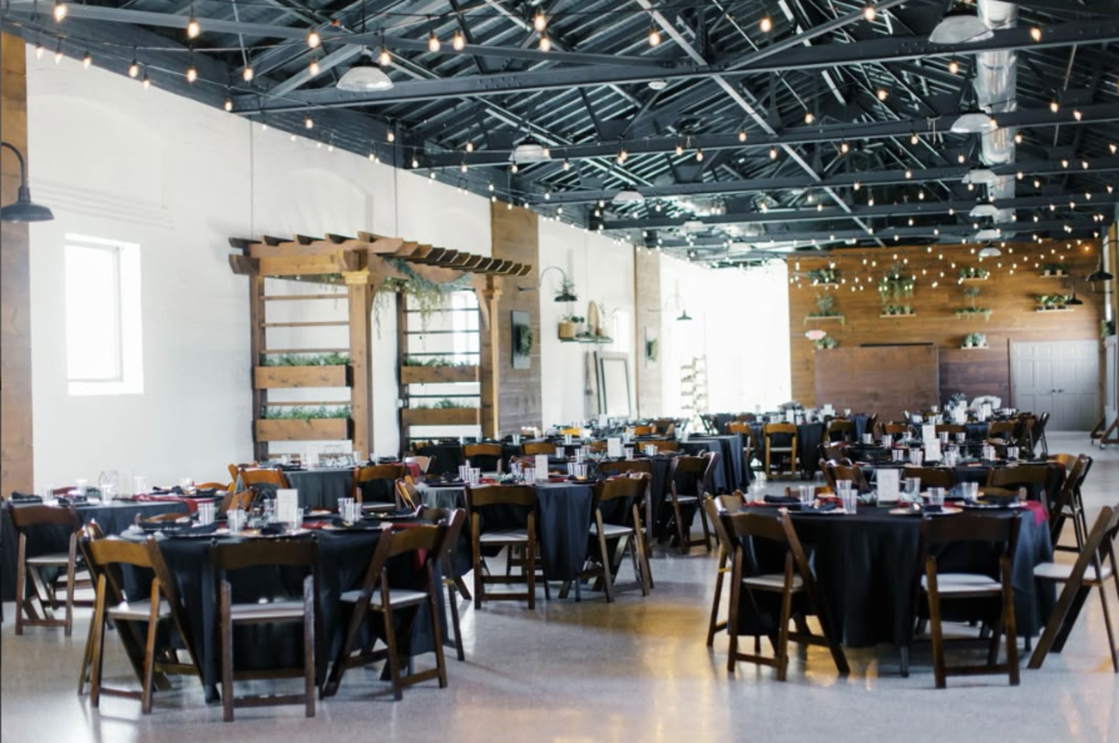 The Silk Mill on Main Wedding Reception Space in New Holland, PA Industrial wedding reception space at The Silk Mill on Main in New Holland, PA, featuring exposed steel beams, string lights, and round reception tables.