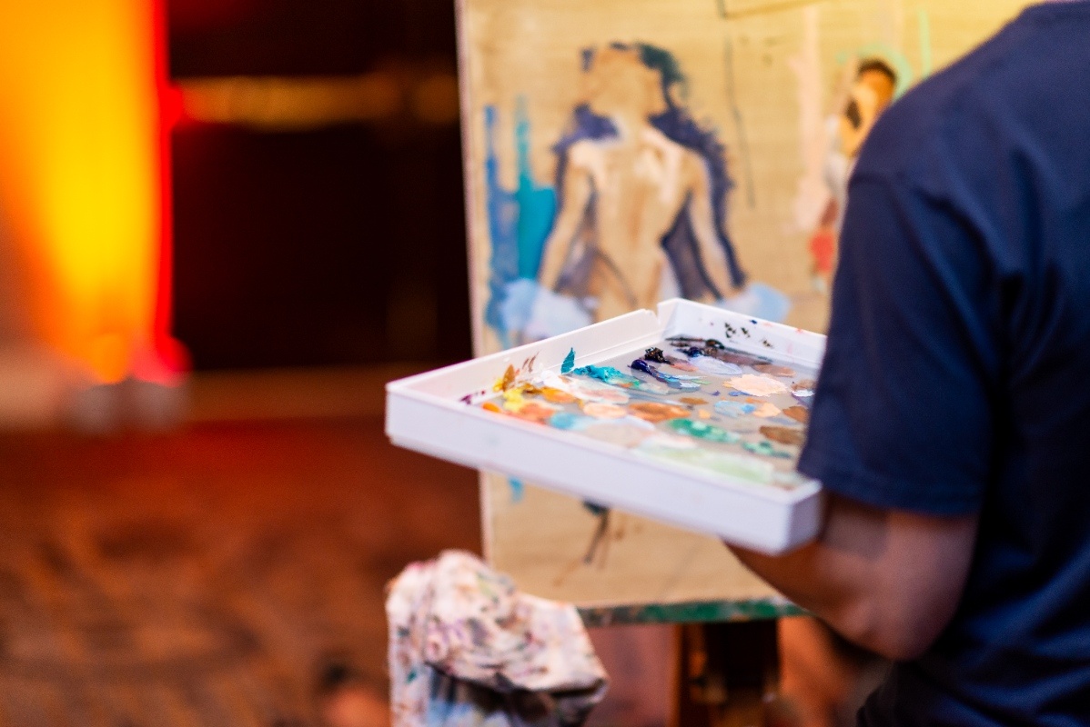 A live artist paints a wedding scene using a colorful palette during the Oklahoma!-inspired styled shoot, adding an interactive and creative touch to the event.