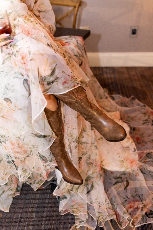 Close-up of a bride wearing brown cowboy boots under a flowing floral wedding gown, blending rustic country style with romantic Oklahoma!-inspired elegance.