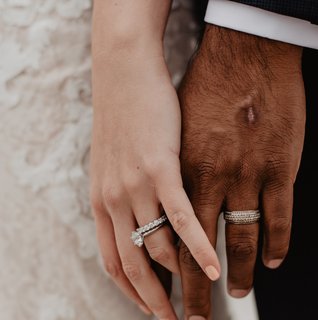 Bride and groom holding hands during a wedding ceremony, featuring close-up wedding rings and lace bridal gown details.