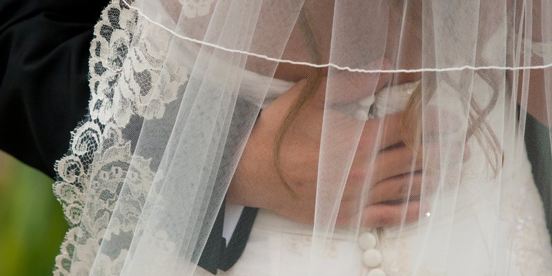 Close-up detail of a bride’s lace-trimmed wedding veil draped softly over her face during a quiet, emotional moment. The delicate ivory lace and sheer tulle create a romantic, timeless bridal look perfect for elegant or classic weddings.