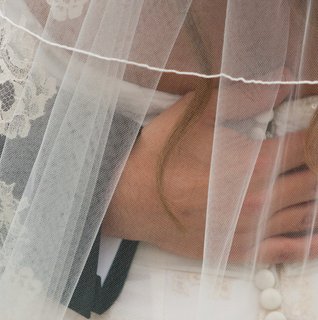 Close-up detail of a bride’s lace-trimmed wedding veil draped softly over her face during a quiet, emotional moment. The delicate ivory lace and sheer tulle create a romantic, timeless bridal look perfect for elegant or classic weddings.