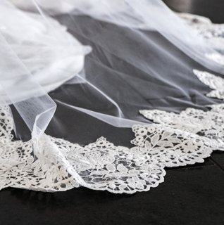 Close-up of a wedding veil with delicate lace trim spread across a dark wooden floor