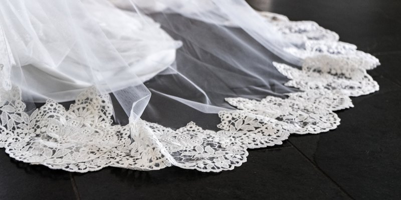 Close-up of a wedding veil with delicate lace trim spread across a dark wooden floor